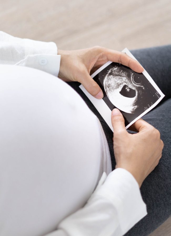 A pregnant woman is looking at an ultrasound photo of fetus. Mother gently touches the baby on stomach.Women are pregnant for 2-3 days or during the first trimester.